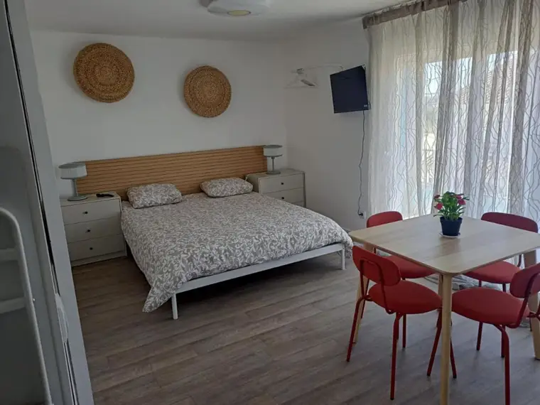 Estúdio com cama de casal, mesa de refeições e cadeiras vermelhas