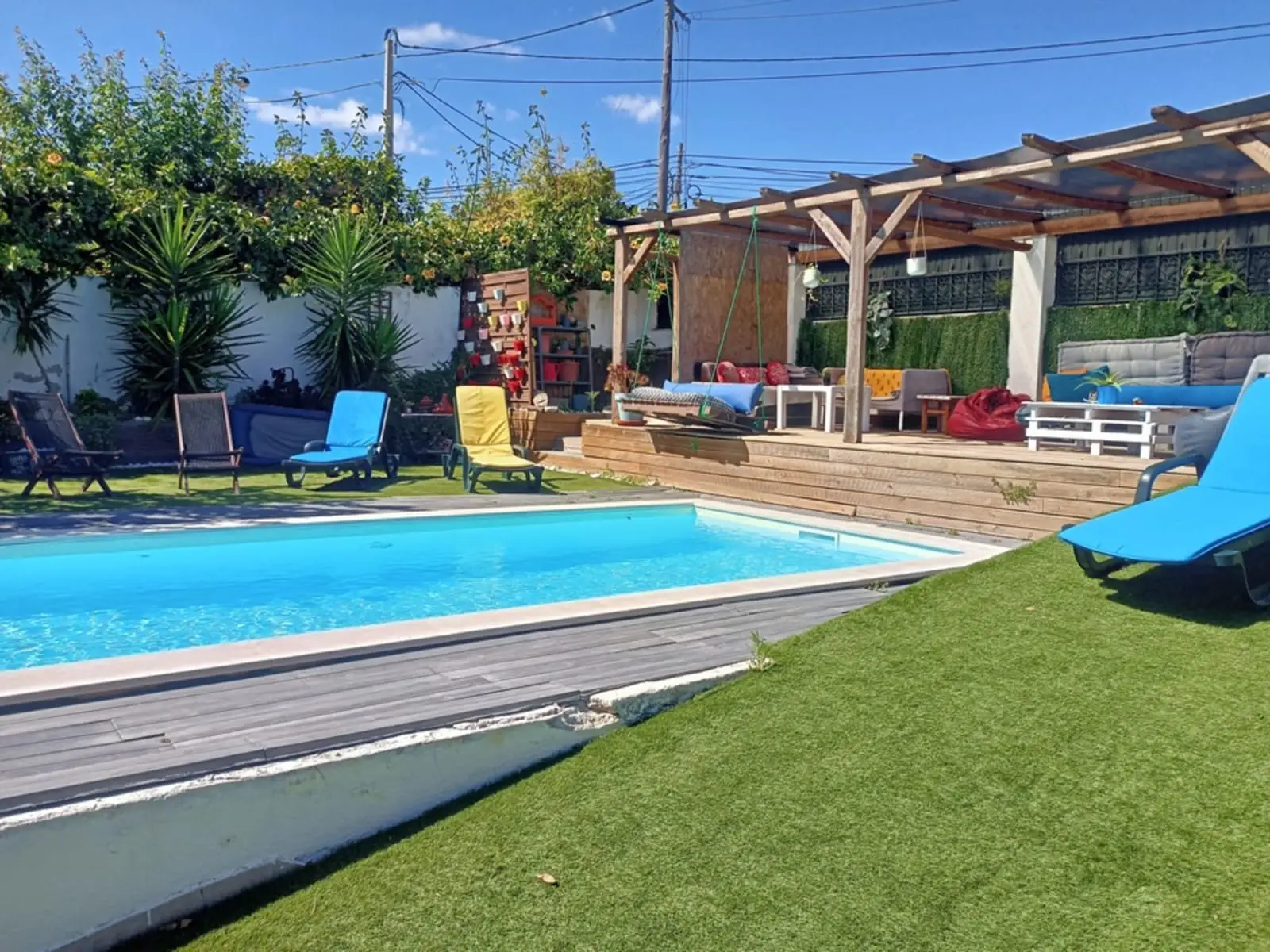 Piscina com deck, pérgula e espreguiçadeiras azuis num dia de sol